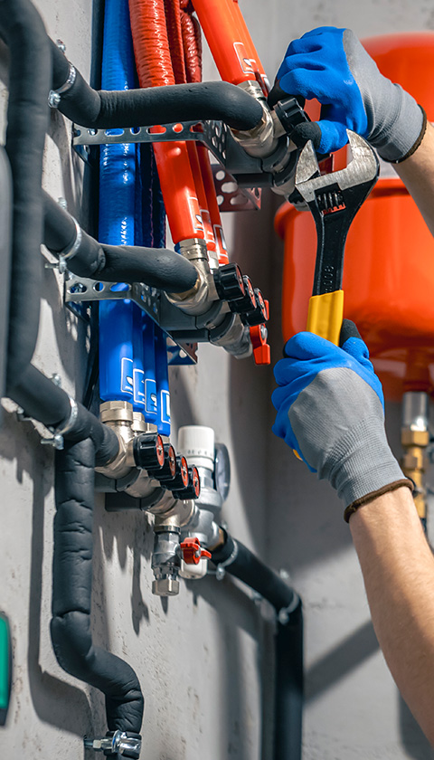 hands using a wrench to adjust plumbing pipes with red and blue hoses demonstrating plumbing maintenance for 14 installations