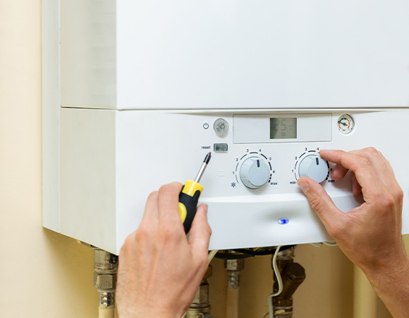 hand adjusting the temperature settings on a white boiler unit with a screwdriver displaying eight different dial options for precise control